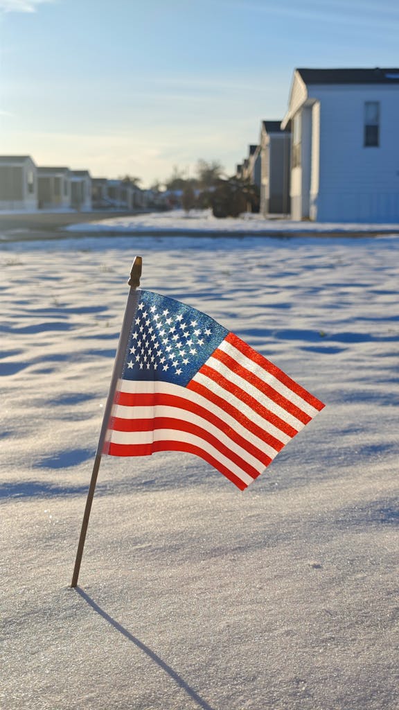 A small American flag stands in the snow within a suburban neighborhood on a sunny winter day.